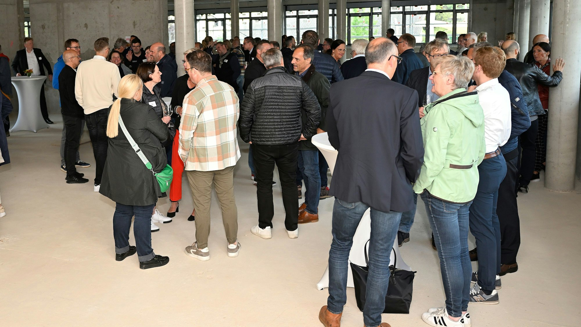 Menschen stehen in Jacken und Mänteln in einem Rohbau zusammen und unterhalten sich.