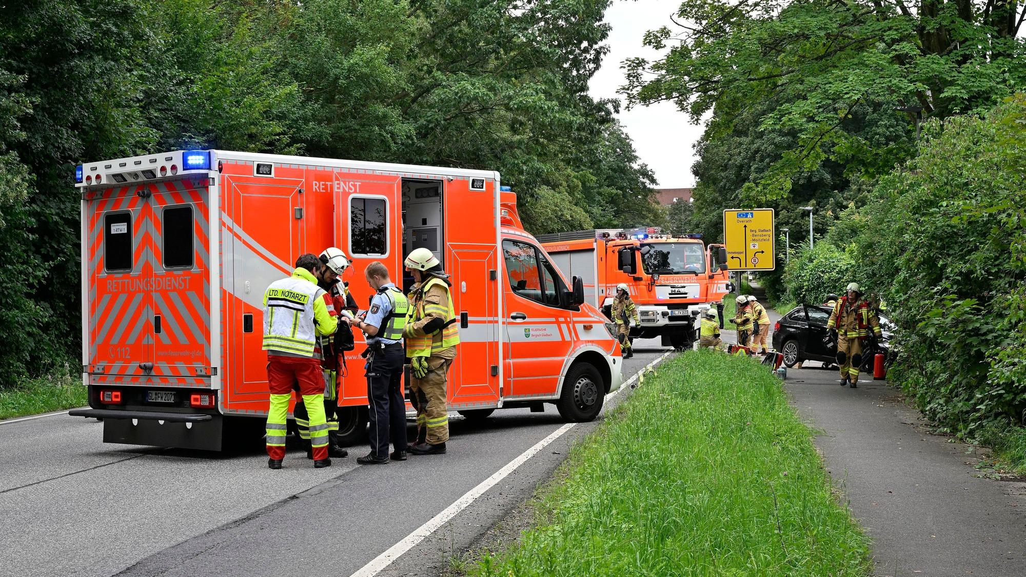 Ein Rettungswagen und ein Feuerwehrauto stehen auf einer Straße. Einsatzkräfte arbeiten an einem Autowrack.