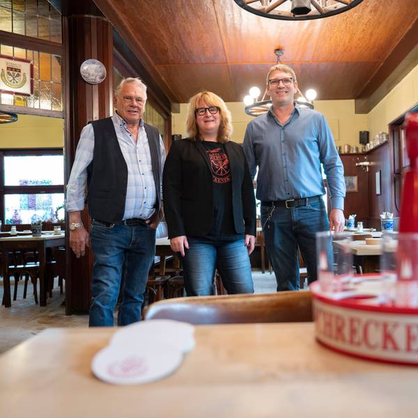 Herrmann-Josef, Brigitte und Georg Wirtz im Portrait, vor ihnen steht ein Kölschkranz auf einem Tisch.