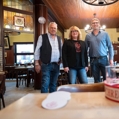 Herrmann-Josef, Brigitte und Georg Wirtz im Portrait, vor ihnen steht ein Kölschkranz auf einem Tisch.