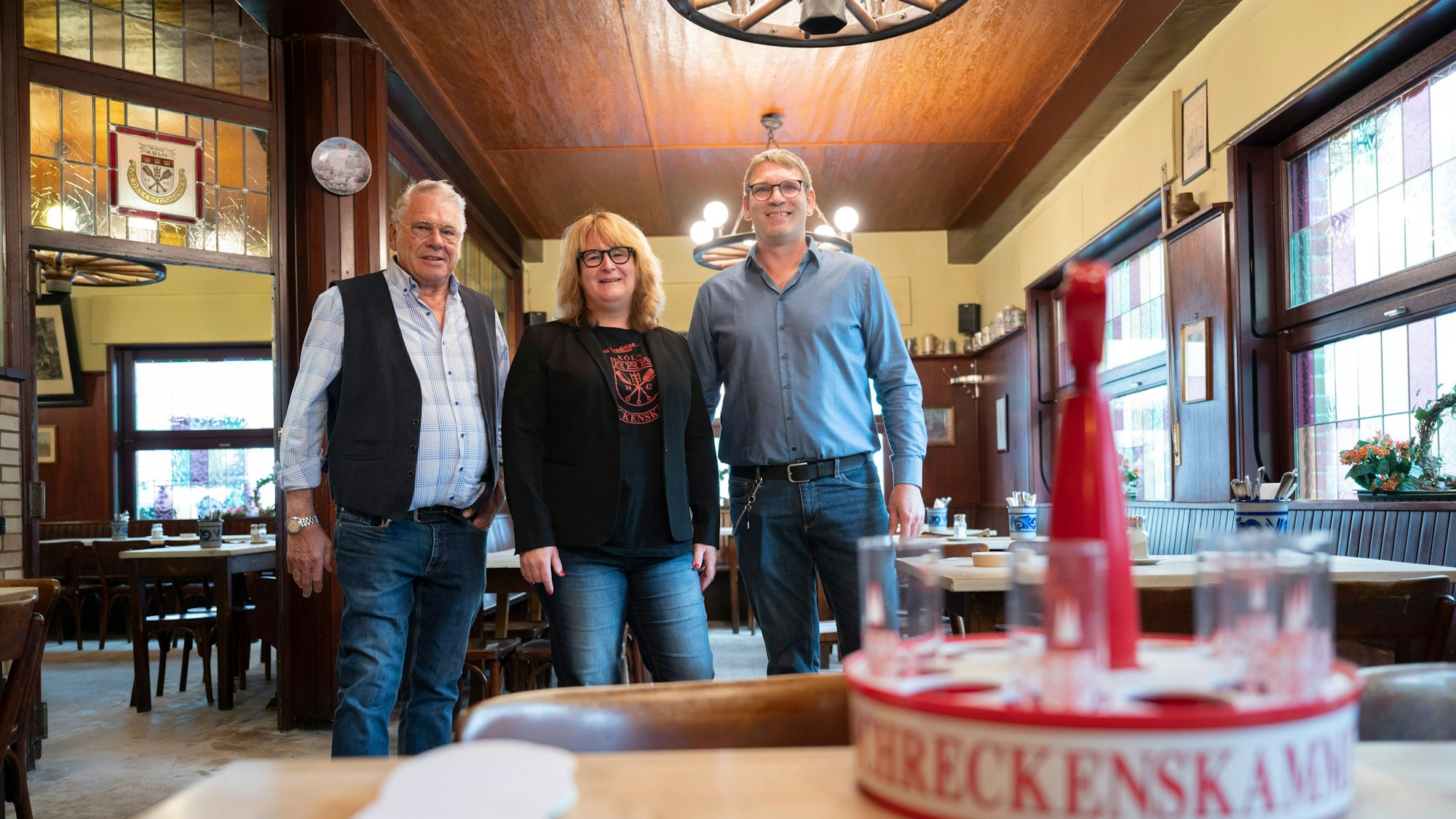 Herrmann-Josef, Brigitte und Georg Wirtz im Portrait, vor ihnen steht ein Kölschkranz auf einem Tisch.