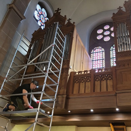 Der Orgelbauer kniet auf einem Gerüst in mehreren Metern Höhe.