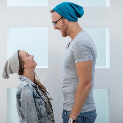 Eine kleine Frau und ein großer Mann stehen sich eng gegenüber und lachen sich an.