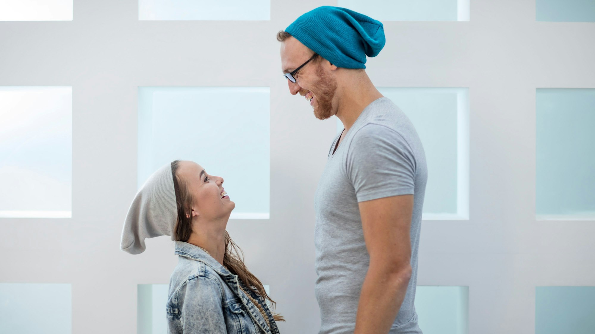 Eine kleine Frau und ein großer Mann stehen sich eng gegenüber und lachen sich an.