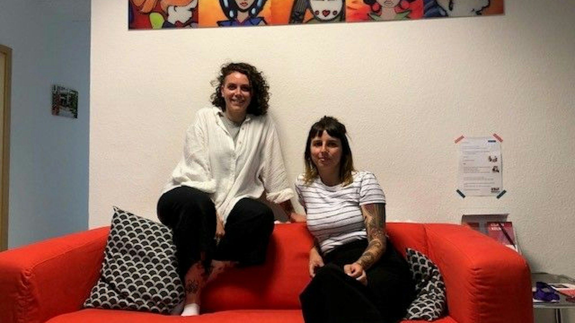 Die Projektleiterinnen Cynthia Hoffmann und Anna Rustler von „Hürden überwinden“ des Kölner Vereins „Lobby für Mädchen“ sitzen auf einem roten Sofa.