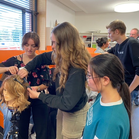 Eine Gruppe von Schülerinnen und Schülern dreht Locken an einem Kunstkopf.