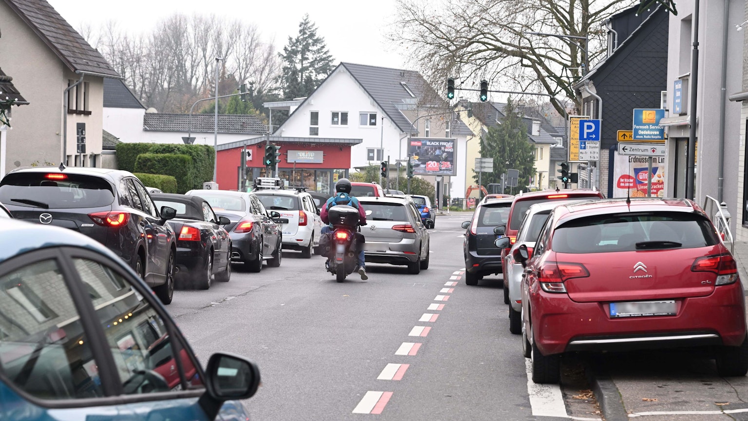 Autos stehen im Stau vor der Ampel. Rechts parken Autos entlang der Straße.