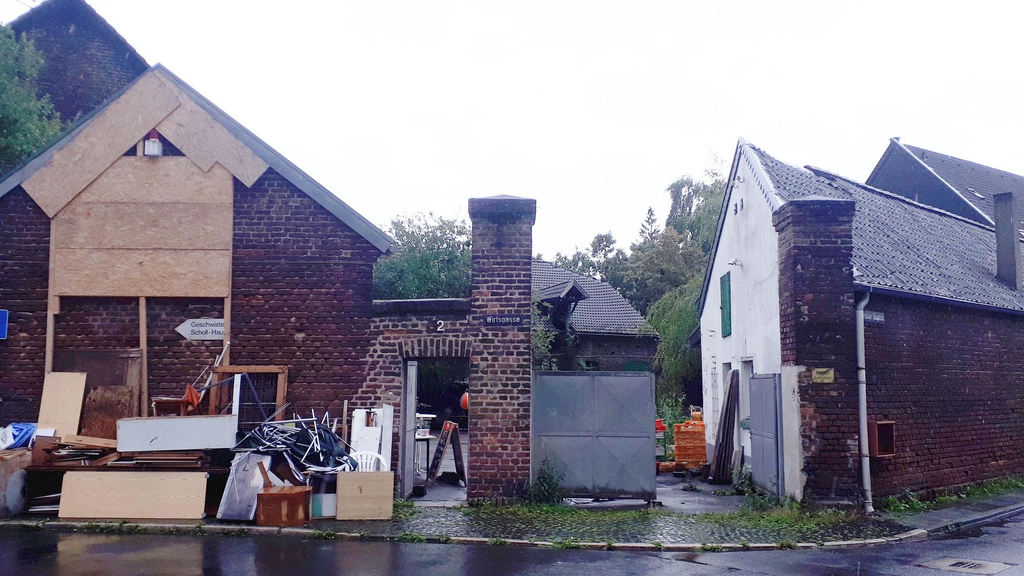 Sperrmüll und Bretter stehen vor einer alten rot verklinkerten Hofanlage.