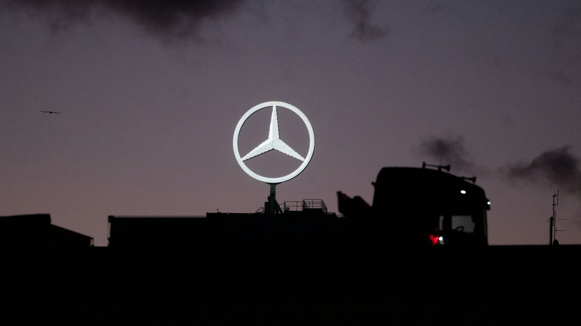 Ein Lastwagen fährt auf einer Brücke, im Hintergrund ist der Mercedes-Stern im Werk Untertürkheim der Daimler AG zu sehen.