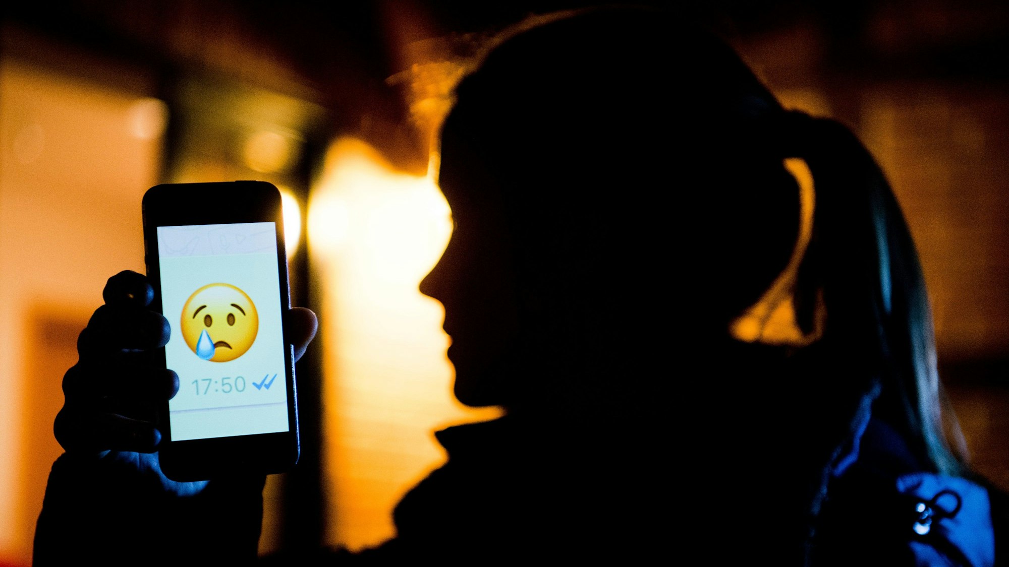 Ein junges Mädchen zeigt das Display eines Smartphones mit einem weinenden Emoji bem Messenger «WhatsApp» (gestellte Szene).