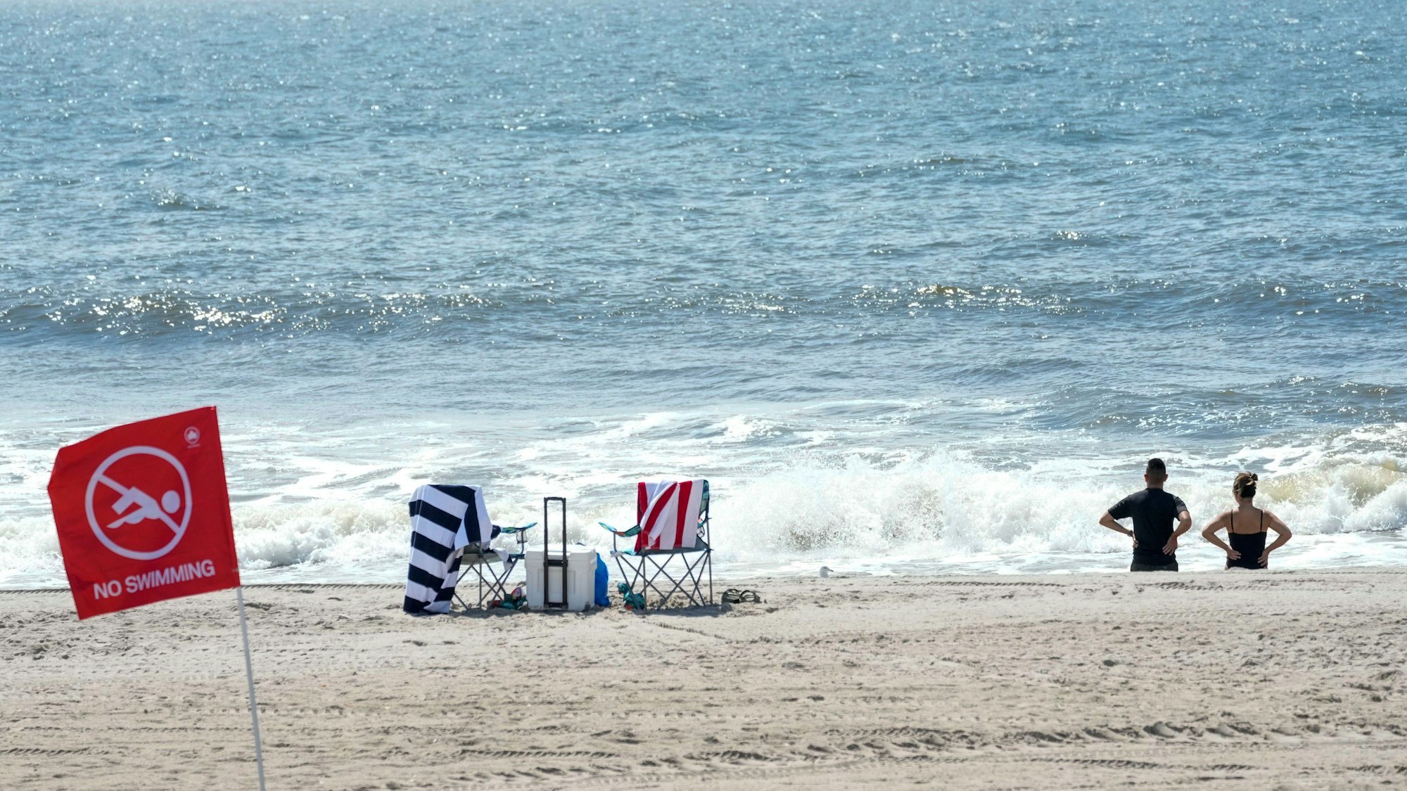 Besucher stehen am Strand vor einer roten Fahne, die für ein Badeverbot am Strand von Rockaway steht.
