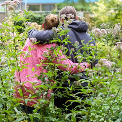 Svanja und Johann stehen in einem Garten, sie stehen mit dem Rücken zur Kamera und haben je einen Arm umeinander gelegt.