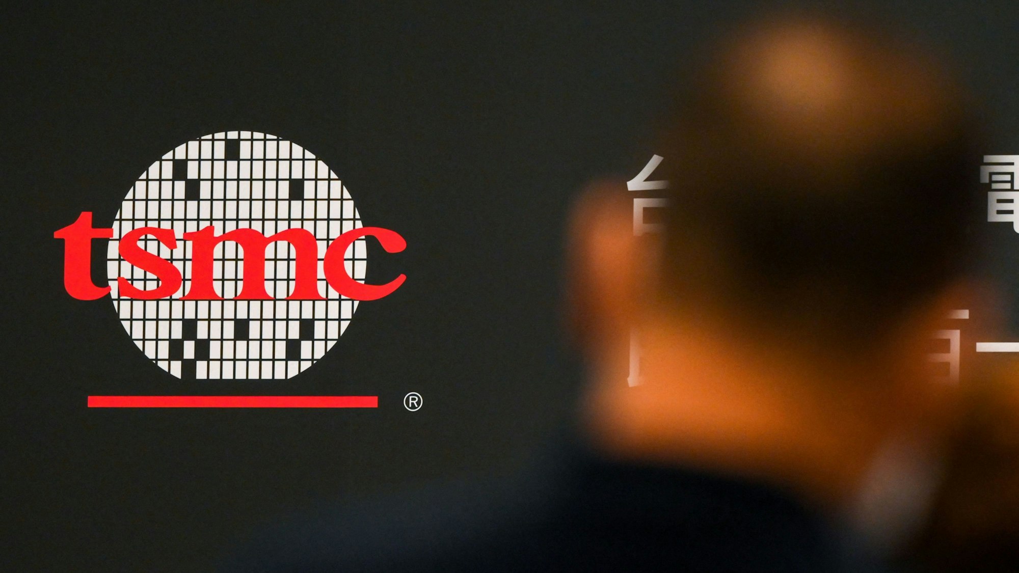 Eine Person vor dem Logo von Taiwan Semiconductor Manufacturing Co., Ltd. (TSMC).