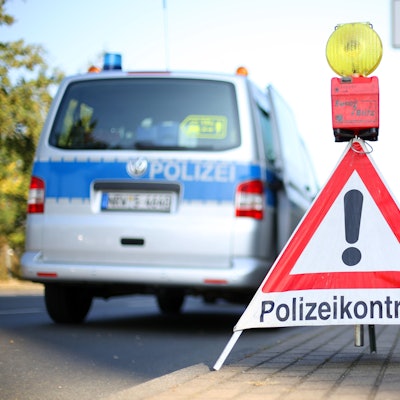 Ein Schild mit der Aufschrift Polizeikontrolle steht vor einem Einsatzwgen der Polizei