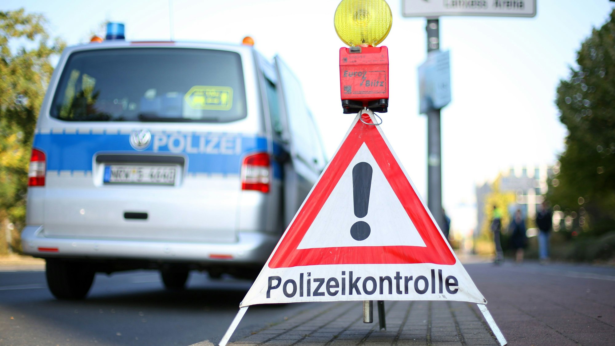 Ein Schild mit der Aufschrift Polizeikontrolle steht vor einem Einsatzwgen der Polizei