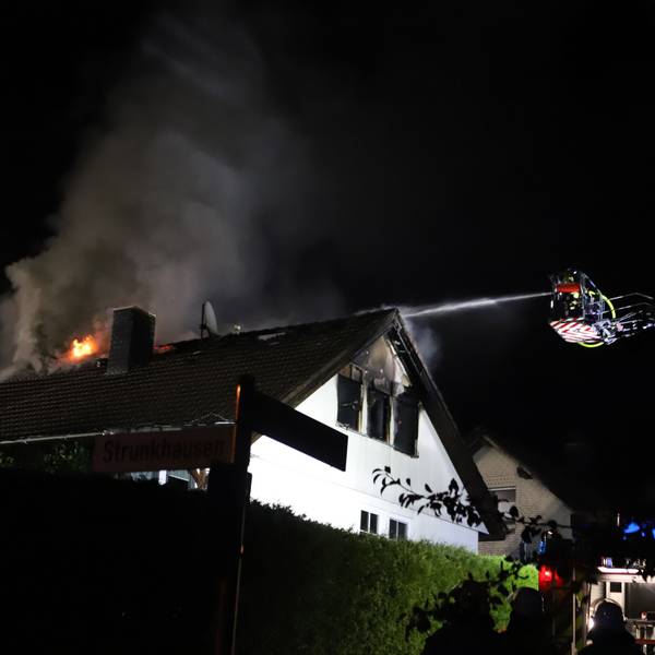 In einem frei stehenden Einfamilienhaus in Marienfeld ist in der Nacht vom 1. auf den 2. August das Dachgeschoss komplett ausgebrannt. Von der Drehleiter aus löschen Feuerwehrleute die Flammen.