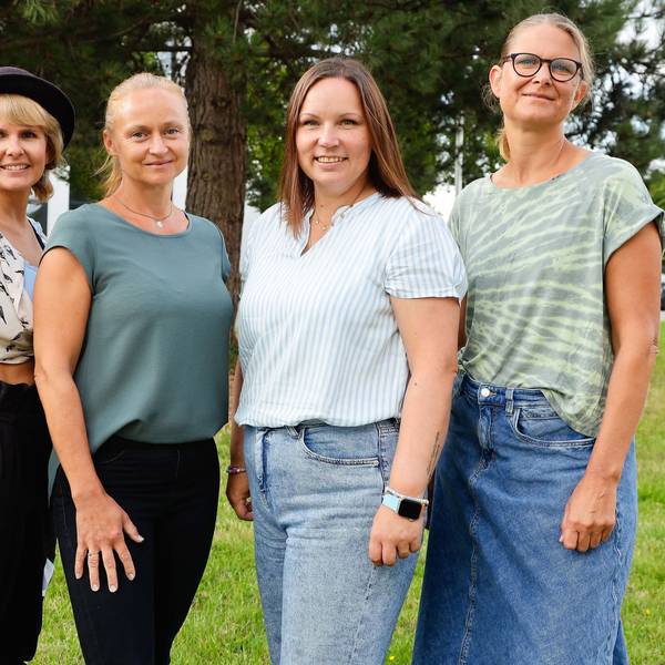 Vier Frauen stehen auf einer Weise vor einem Baum.