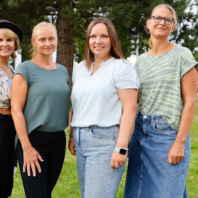 Vier Frauen stehen auf einer Weise vor einem Baum.
