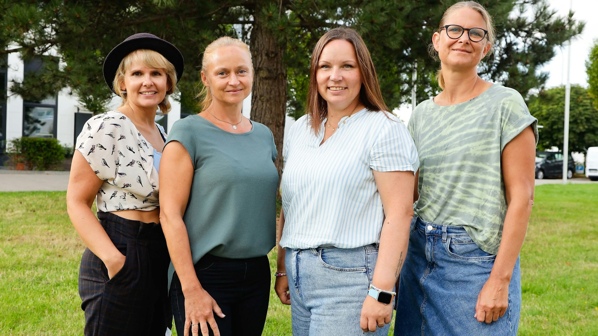 Vier Frauen stehen auf einer Weise vor einem Baum.
