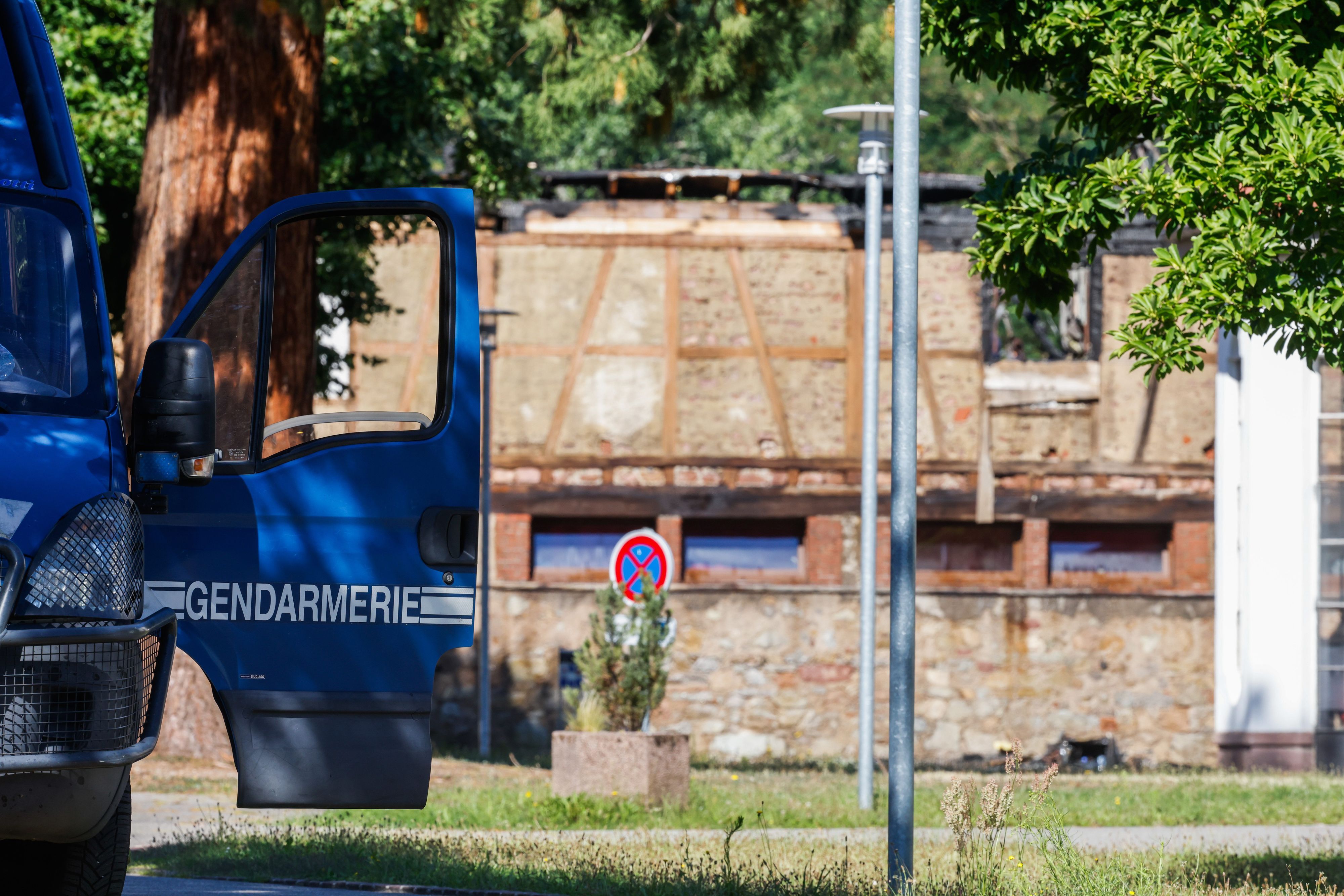 Die Tür eines Fahrzeugs der Gendarmerie steht offen, während im Hintergrund ein Haus zu sehen ist, in dem am Vortag bei einem Feuer elf Menschen ums Leben kamen.