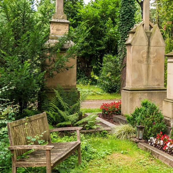 Eine Holzbank steht an einem Grab auf dem Melatenfriedhof.