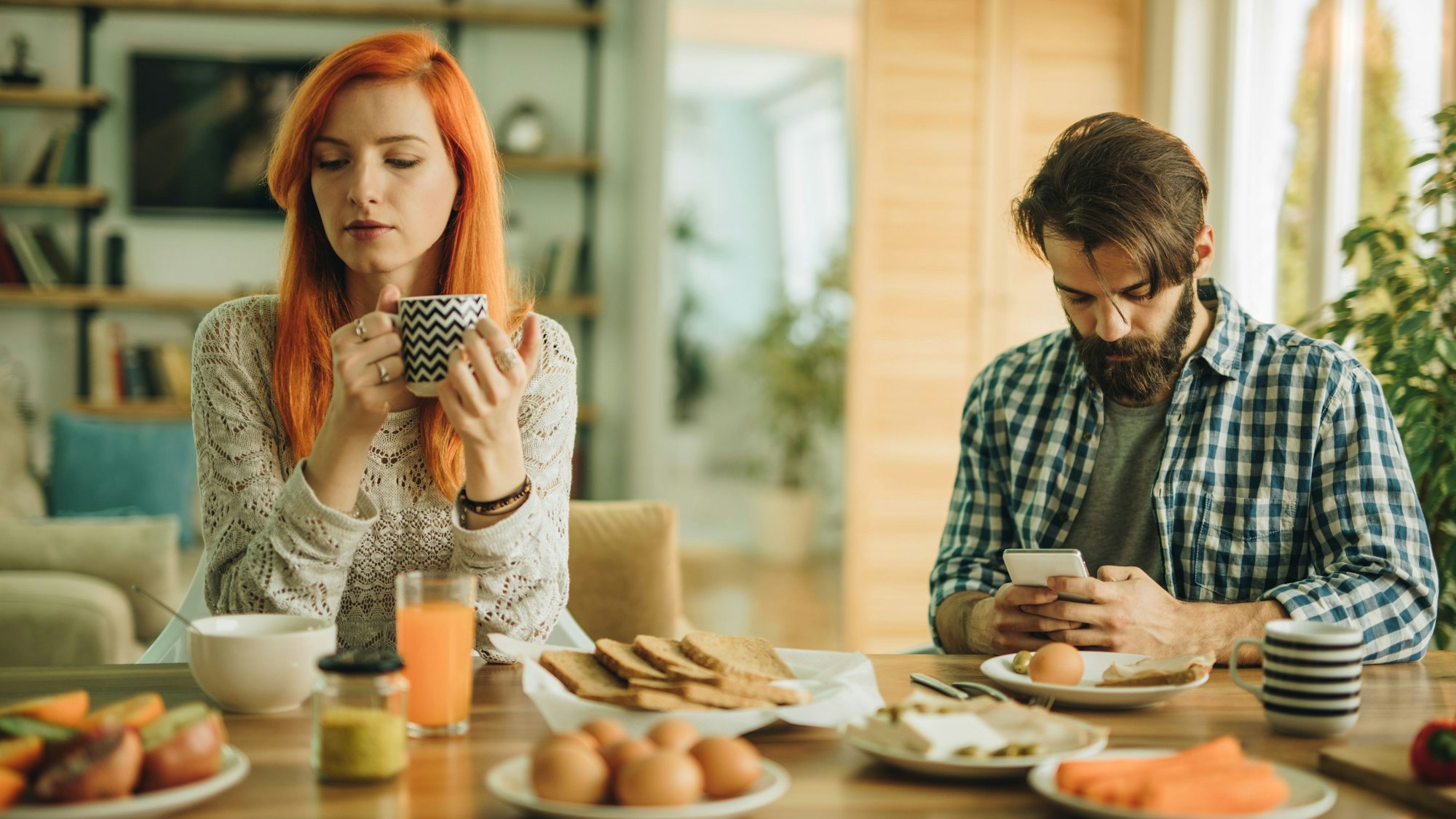 Mann und Frau beim Frühstück. Mann ist abgelenkt vom Smartphone.