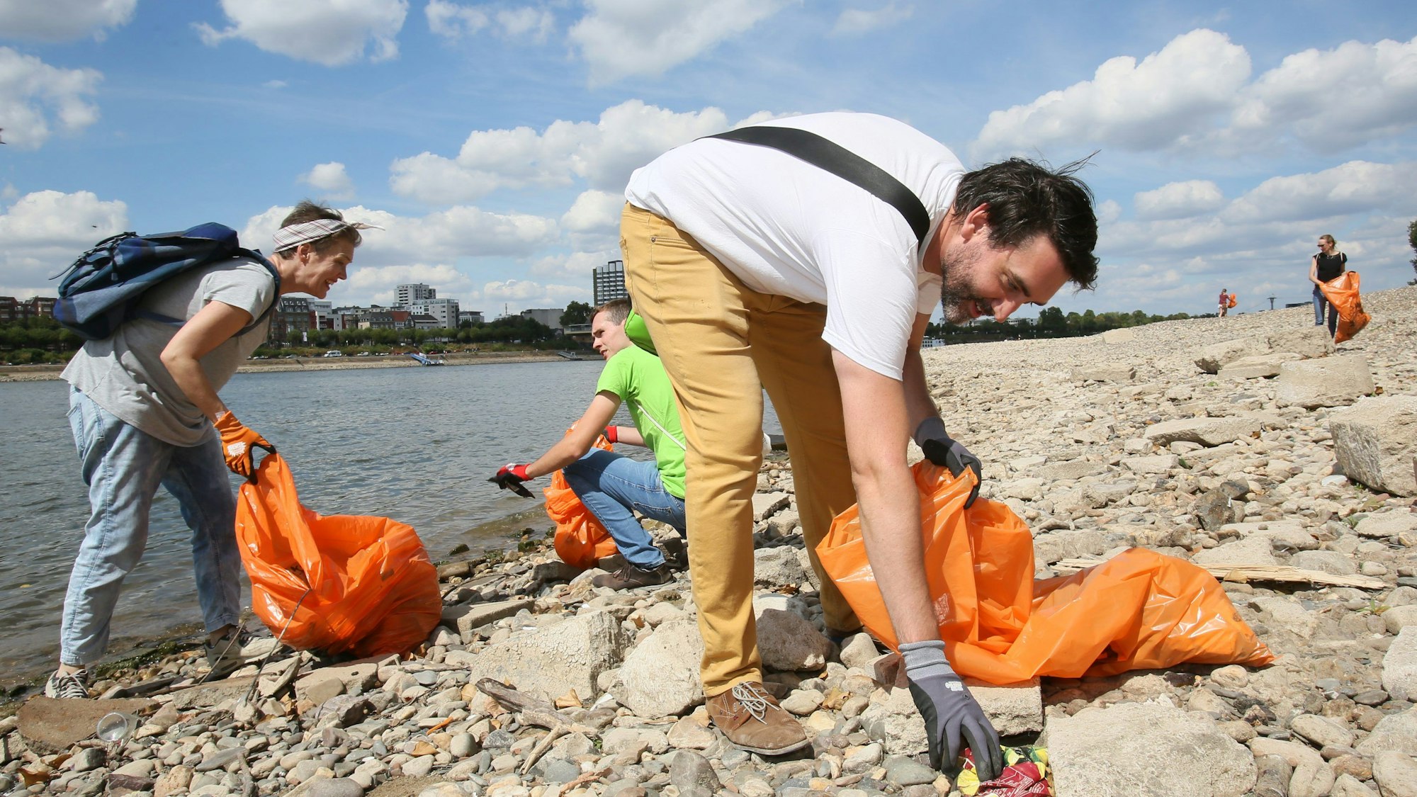 Christian Stock von dem Verein Krake sammelt Müll am Rheinufer in einem orangen Müllbeute.