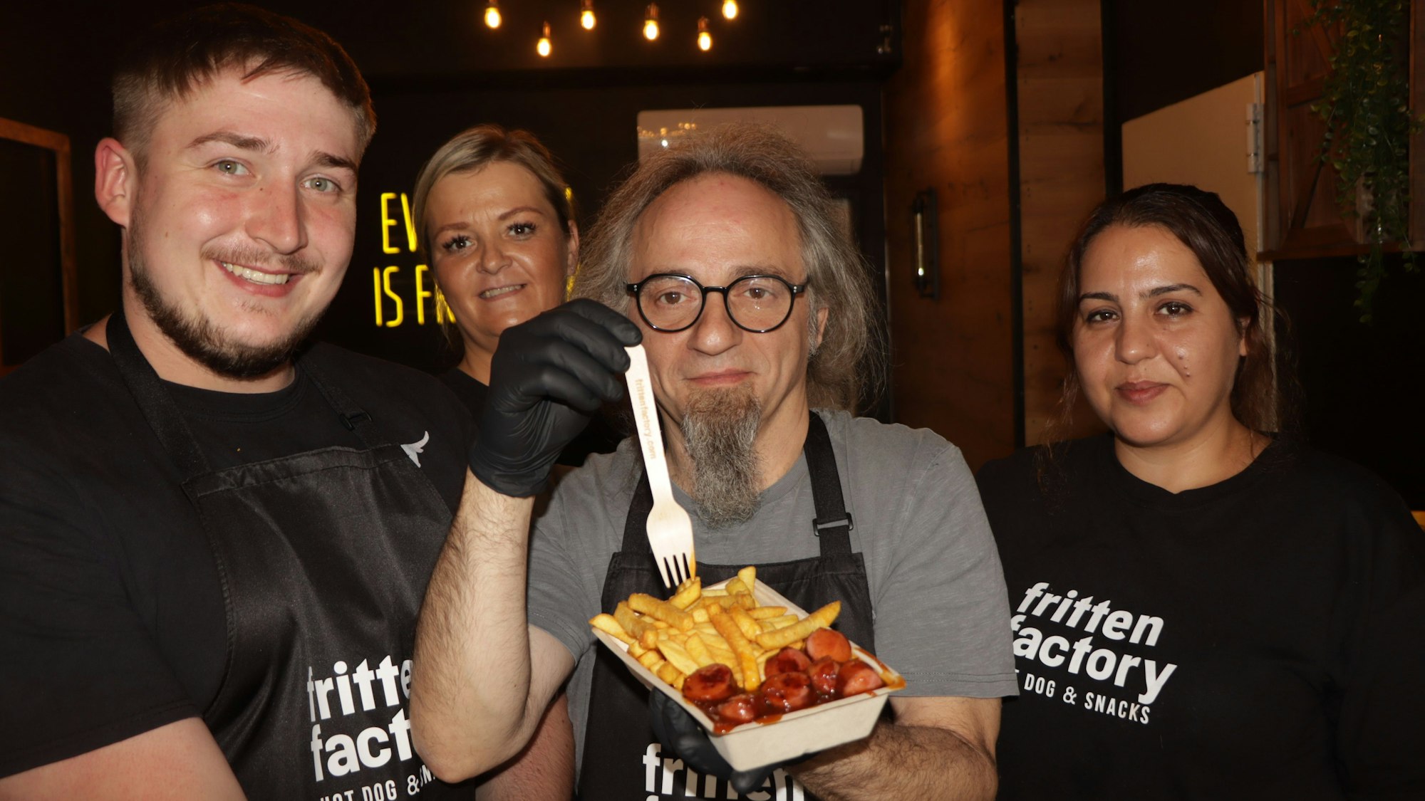Ein Mann hält eine Schale mit Fritten, umgeben von zwei Frauen und einem Mann.