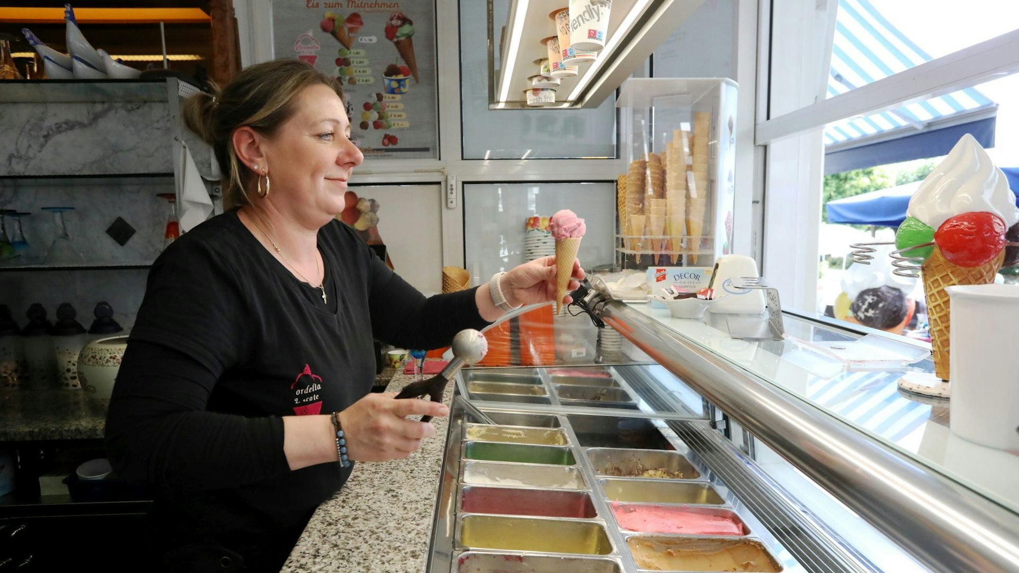 Die Mitarbeiterin einer Eisdiele hält ein Eishörnchen in der Hand.