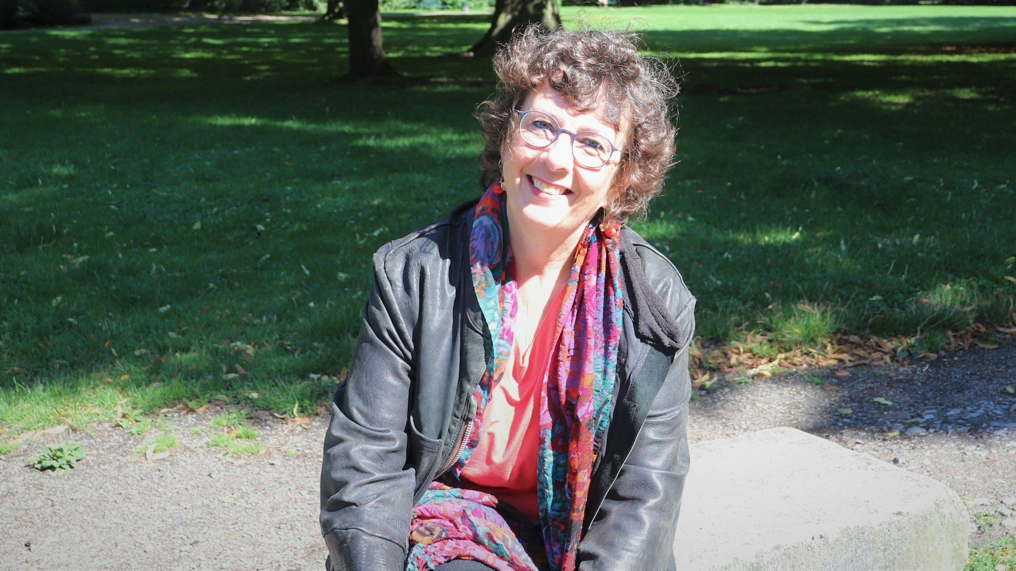 Die Gründerin der Kölner „Familienhörbuch gGmbH“ sitzt auf einer Bank aus Stein.