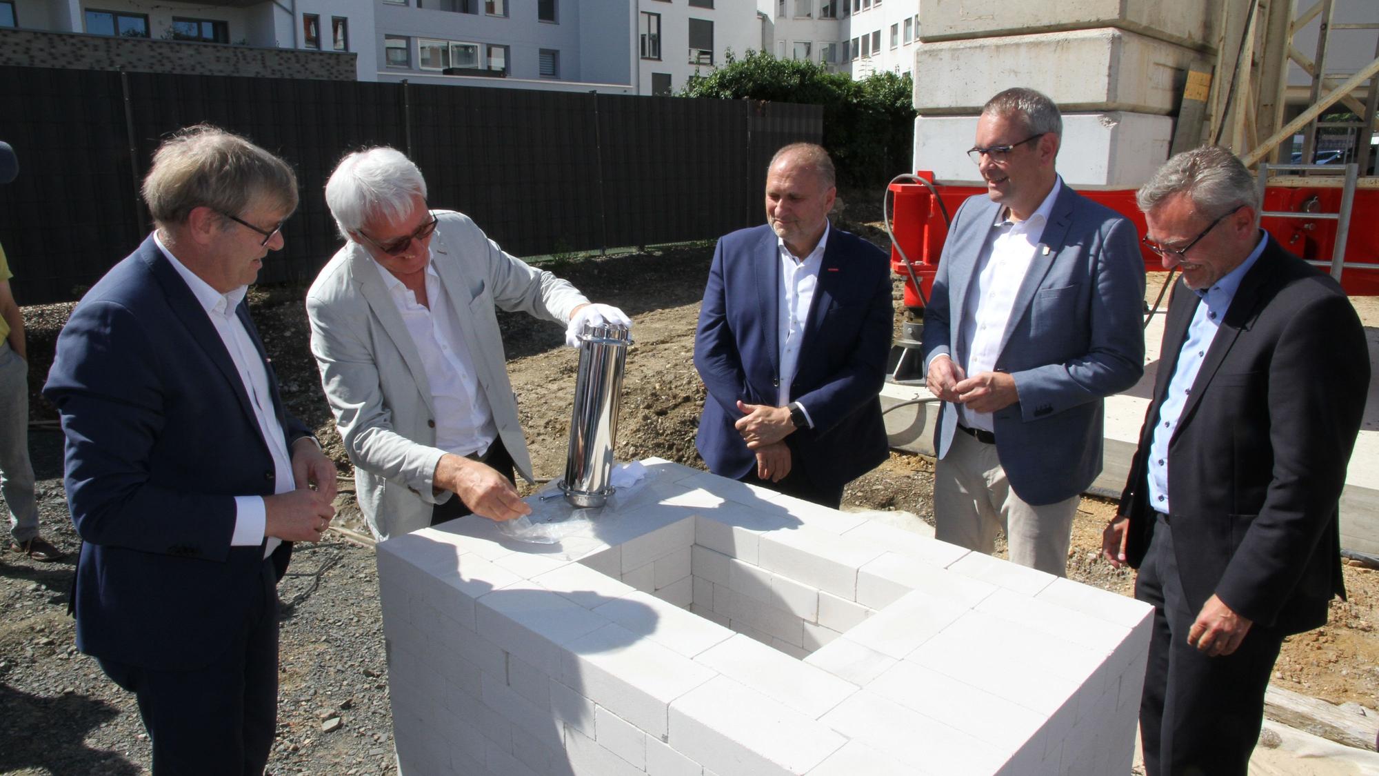 Fünf Männer stehen um ein weißes Mauerwerk für einen Grundstein herum