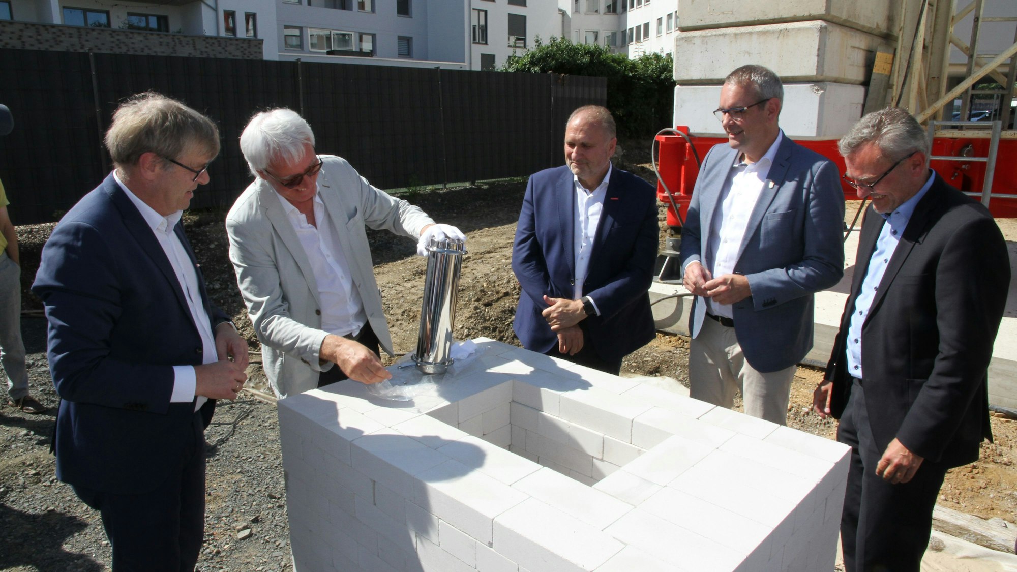 Fünf Männer stehen um ein weißes Mauerwerk für einen Grundstein herum