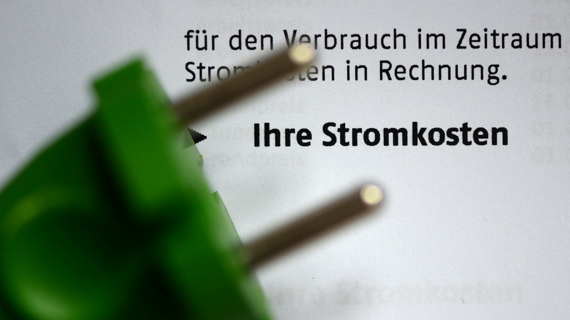 Ein grüner Stromstecker liegt auf einer Stromrechnung.