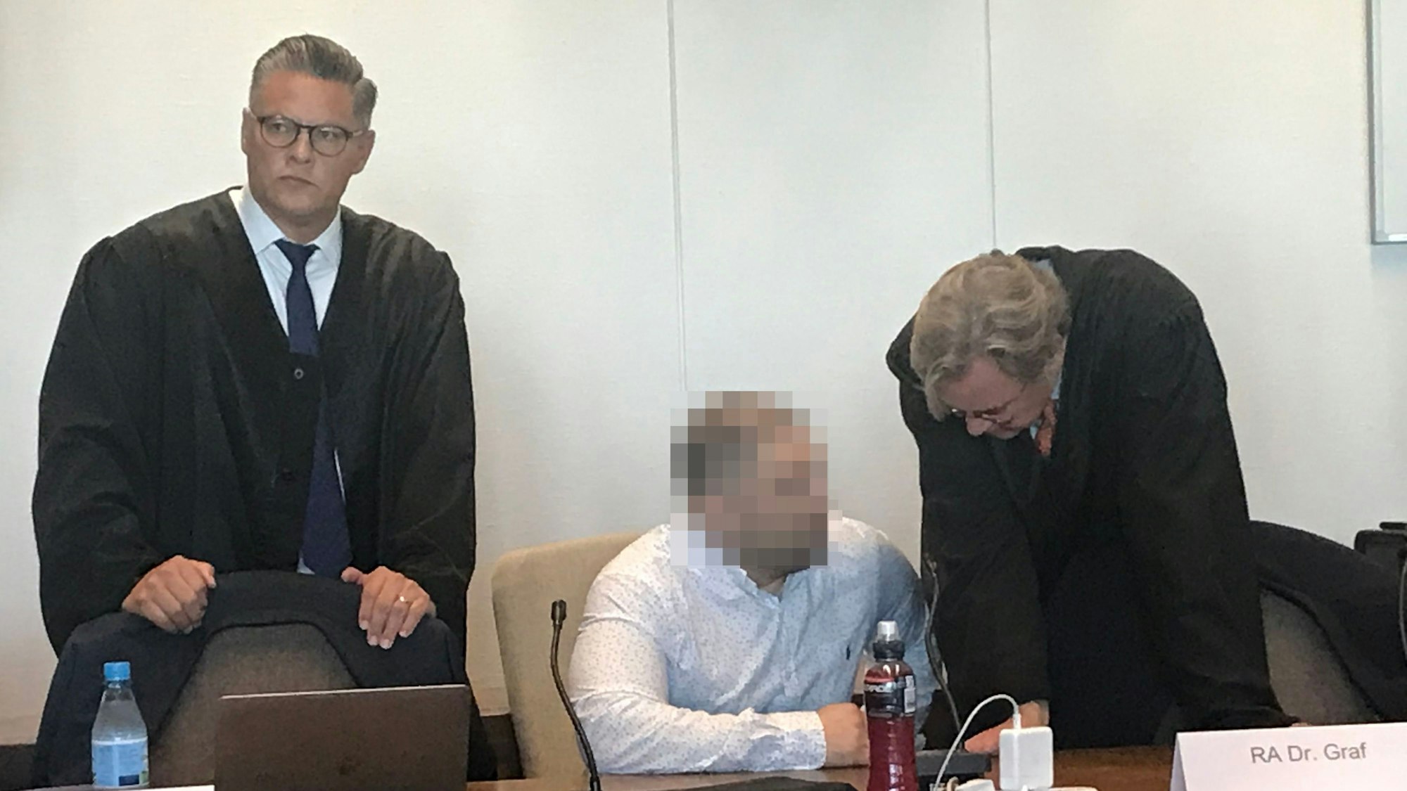 Der Angeklagte sitzt zwischen seinen Verteidigern.