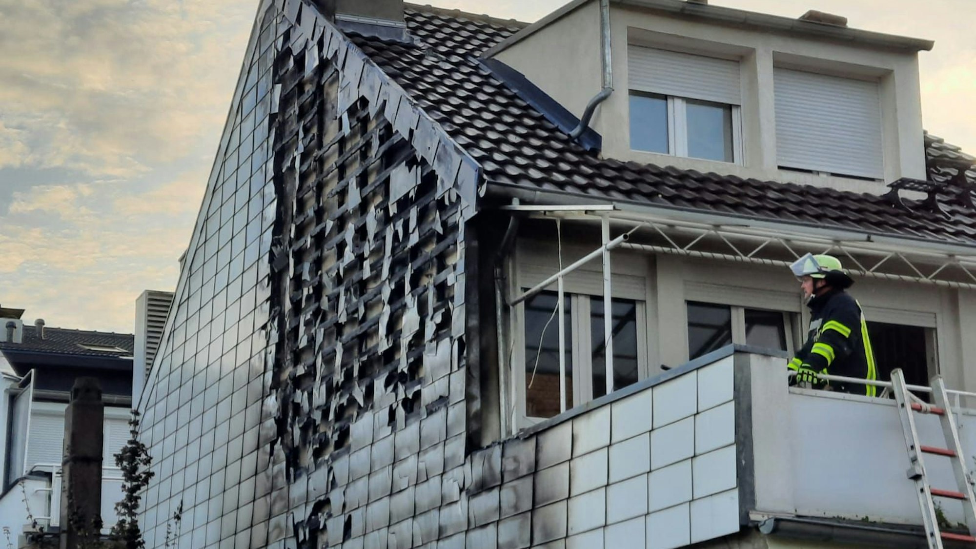 Ein Feuerwehrmann steht auf einem Balkon; links sind die Brandschäden an der Hausfassade zu erkennen.