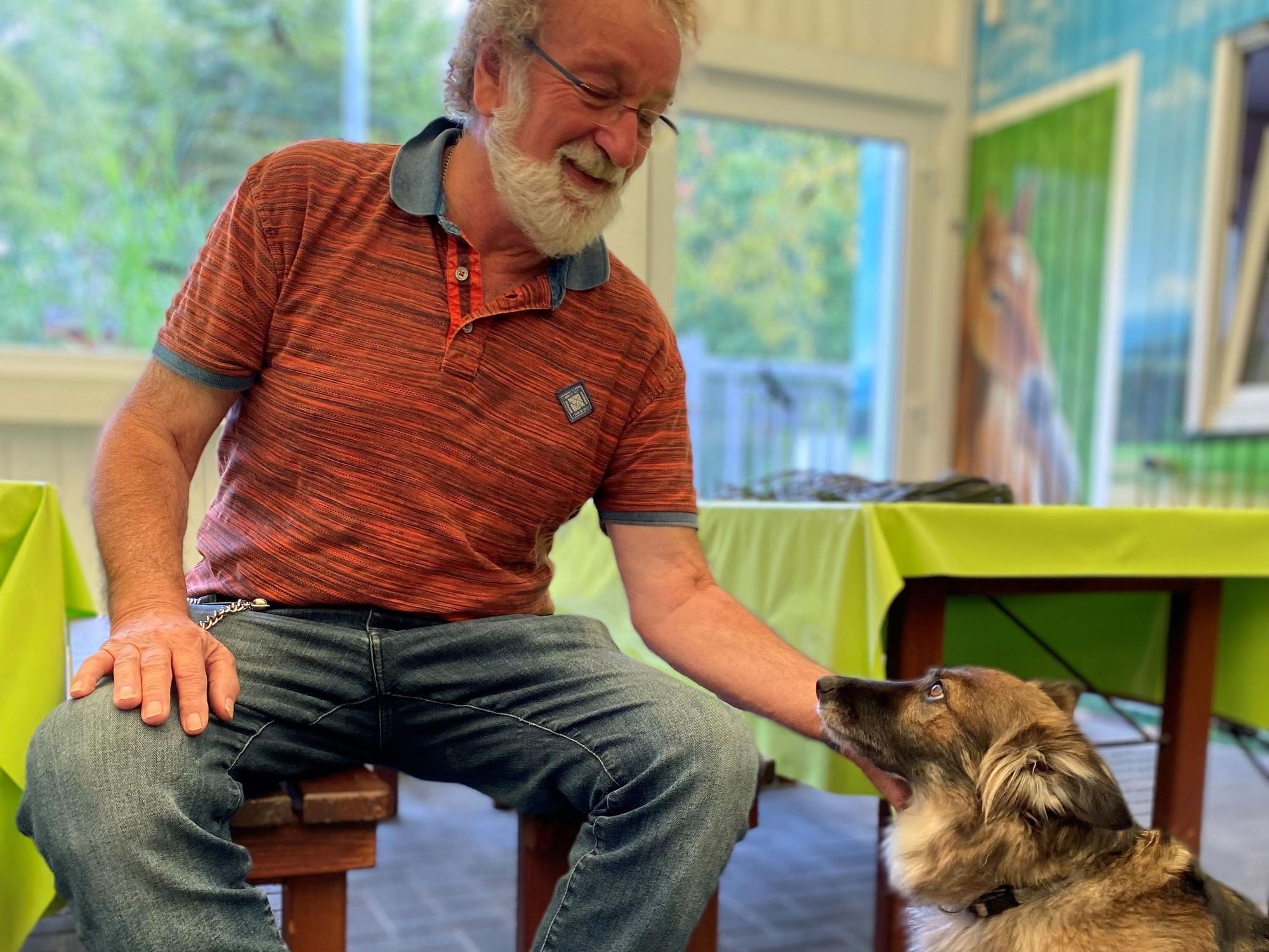 Reiner Bauer sitzt auf einem Stuhl und krault einem Hund den Hals.