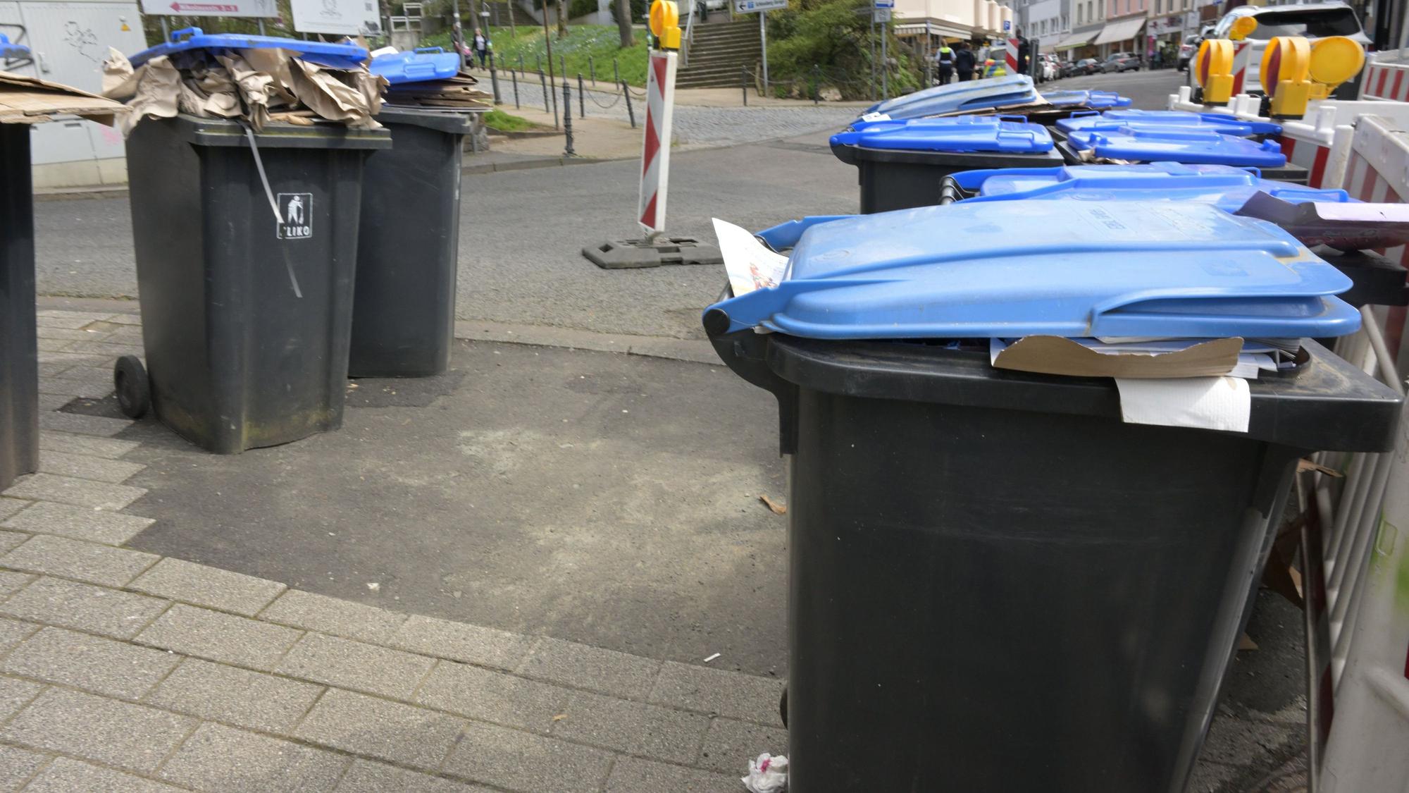 Mehrere blaue Papiertonnen stehen mitten auf der Straße.