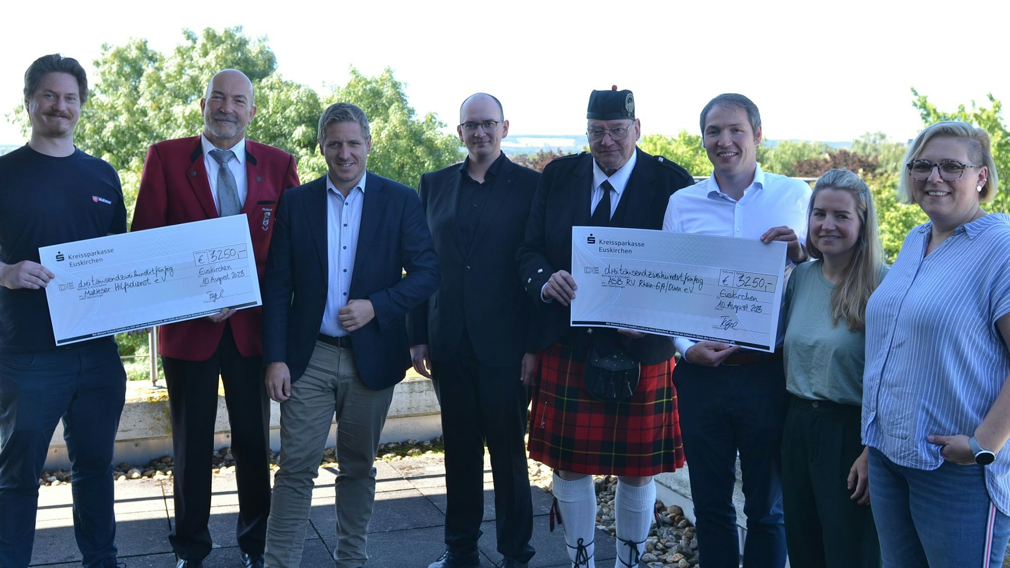 Eine Gruppe Menschen steht zusammen. Sie halten zwei große Schecks, auf denen jeweils 6250 Euro an Spenden für Fluthilfeorganisationen ausgewiesen sind.