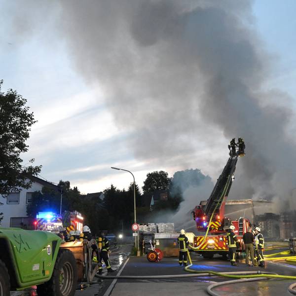 Rauchwolken und Flammen schlagen aus einem Gebäude in den Abendhimmel. Die Feuerwehr löscht den Brand.