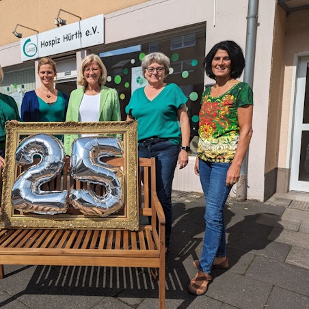 Vier Frauen stehen hinter einer Bank, auf der ein Rahmen mit der silbernen Zahl 25 platziert ist.