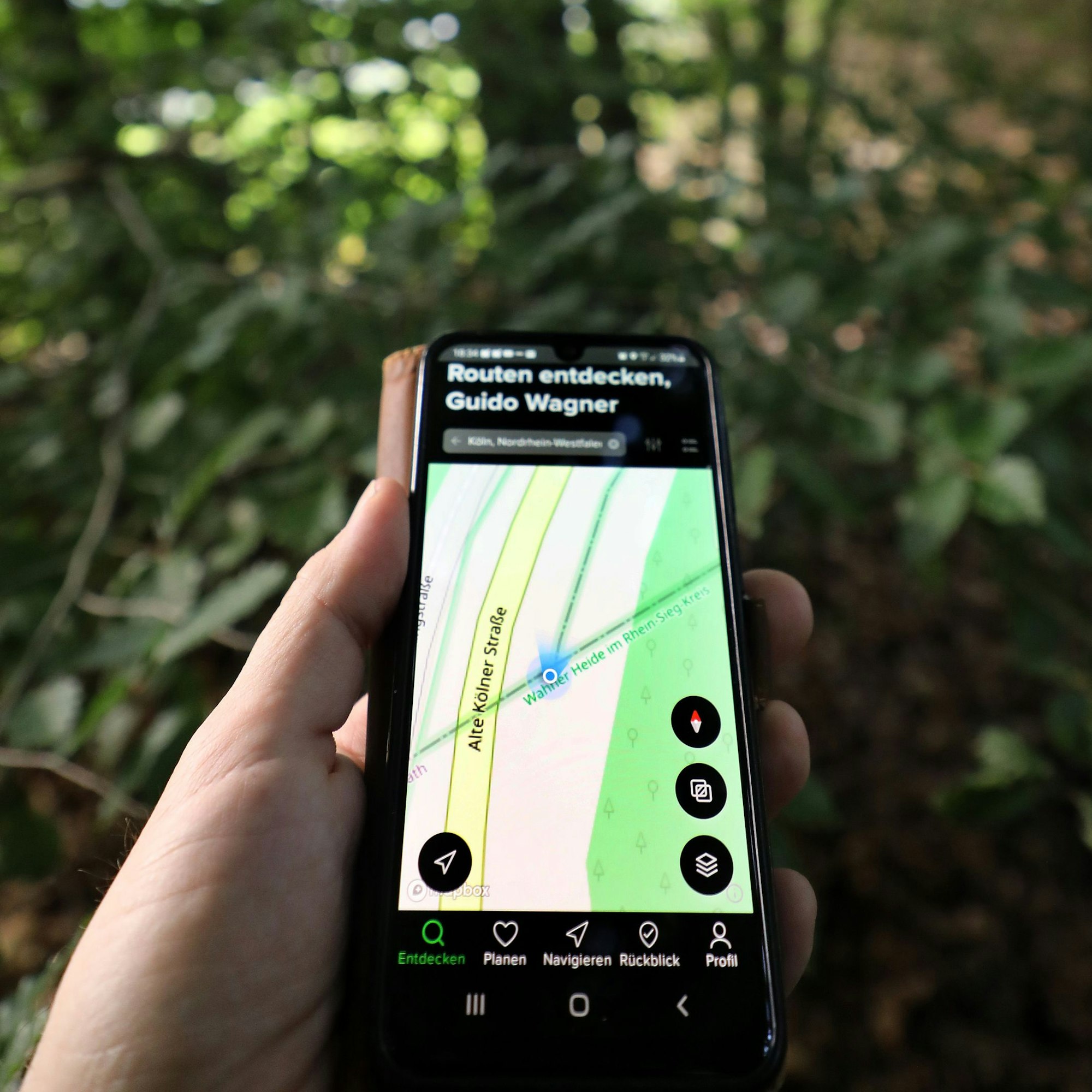 Eine Hand hält ein Handy mit Navi-App im Wald.