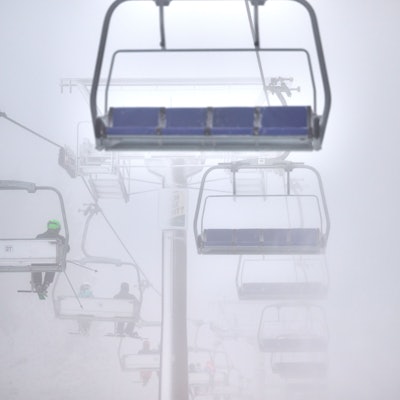 Wintersportler fahren mit einem Sessellift über eine künstlich beschneite Piste. Es ist neblig. (Symbolbild)