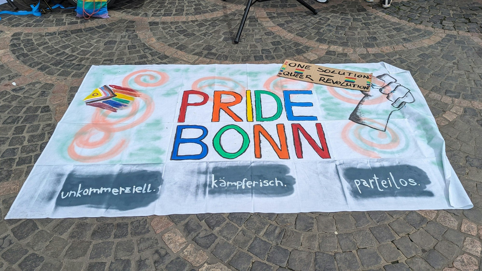 Das Banner der Pride Bonn liegt ausgebreitet auf dem Boden.
