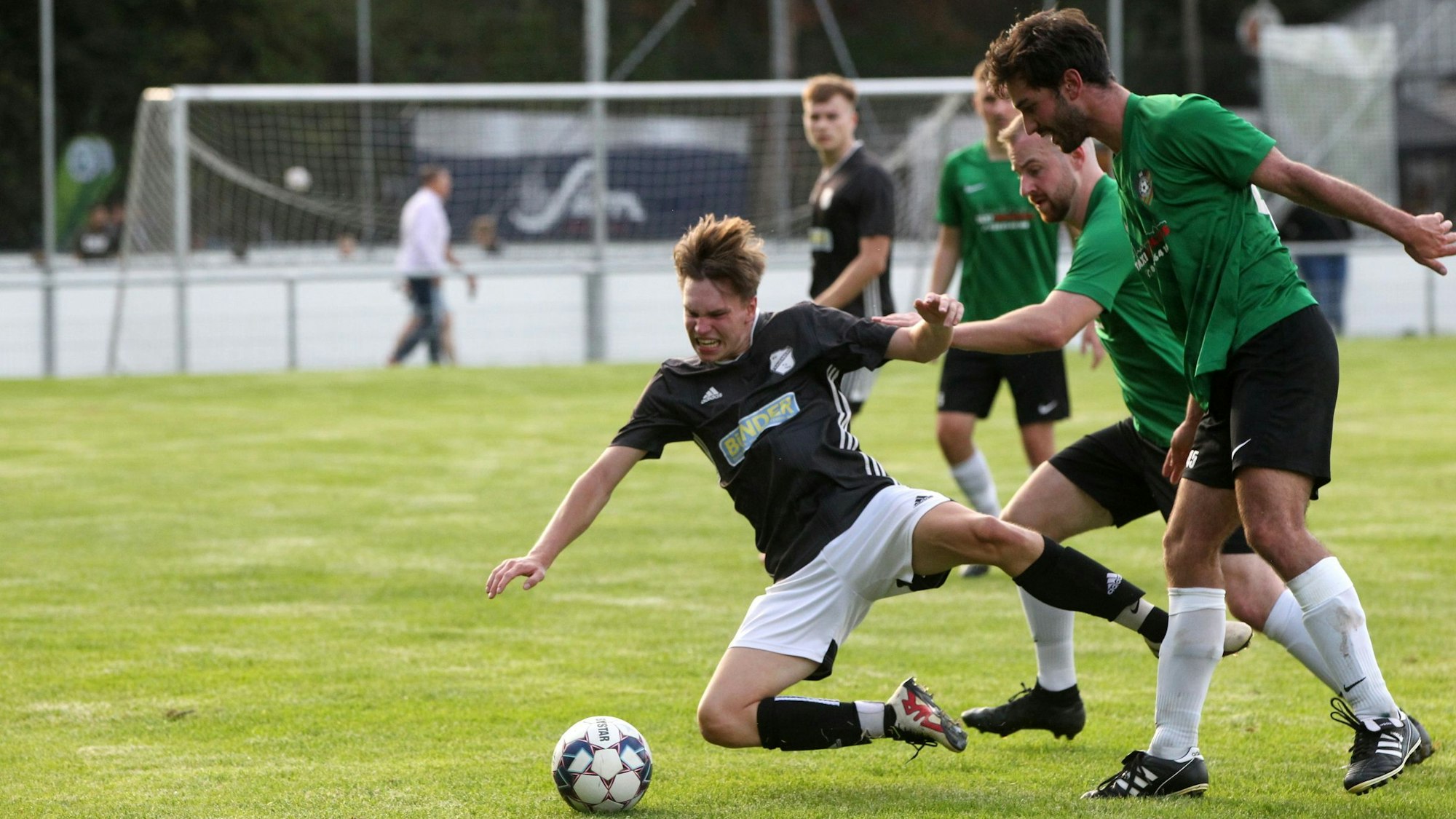 Ein Frauenberger Spieler fällt im Zweikampf mit zwei Spielern von Flamersheim/Kirchheim zu Boden.