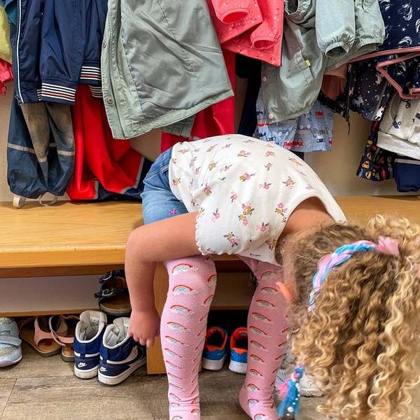 Das Bild zeigt ein Kindergartenkind, das sich auf einer Bank in der Kita die Schuhe anziehen will.