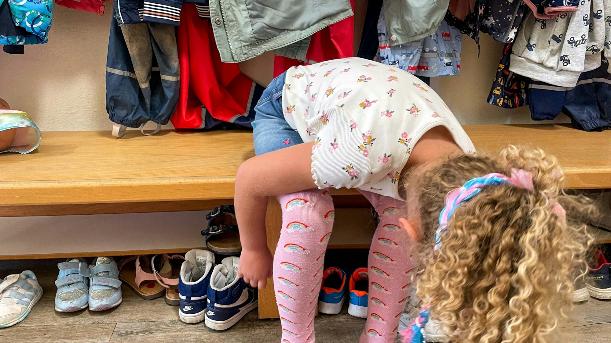 Ein Kita-Kind sitzt auf einer Bank und zieht sich Schlappen an.