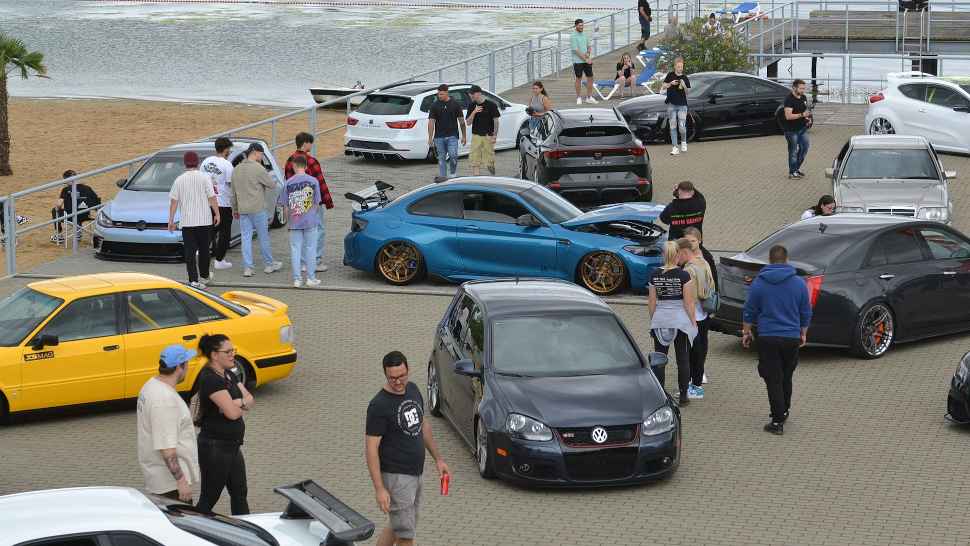 Das Bild zeigt einige getunte Autos vor dem See.