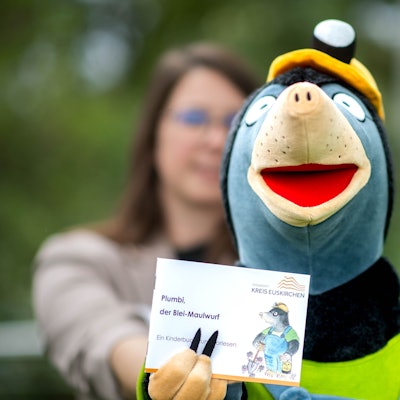 Das Bild zeigt die Handspielfigur Plumbi, die ein kleines Buch in die Kamera hält.