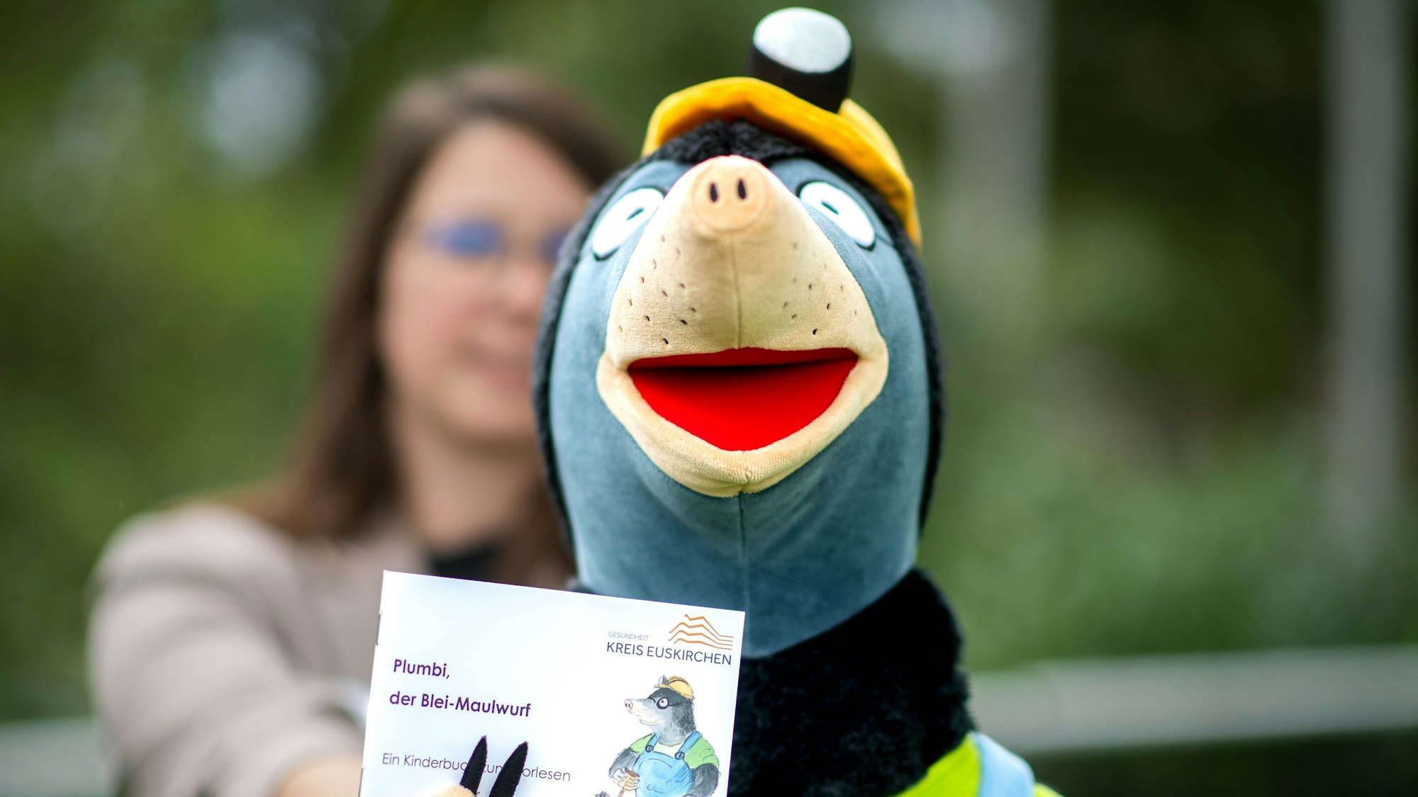 Eine Maulwurf-Stoffpuppe wurde im Bild scharf gestellt, im unscharfen Hintergrund steht eine Frau.