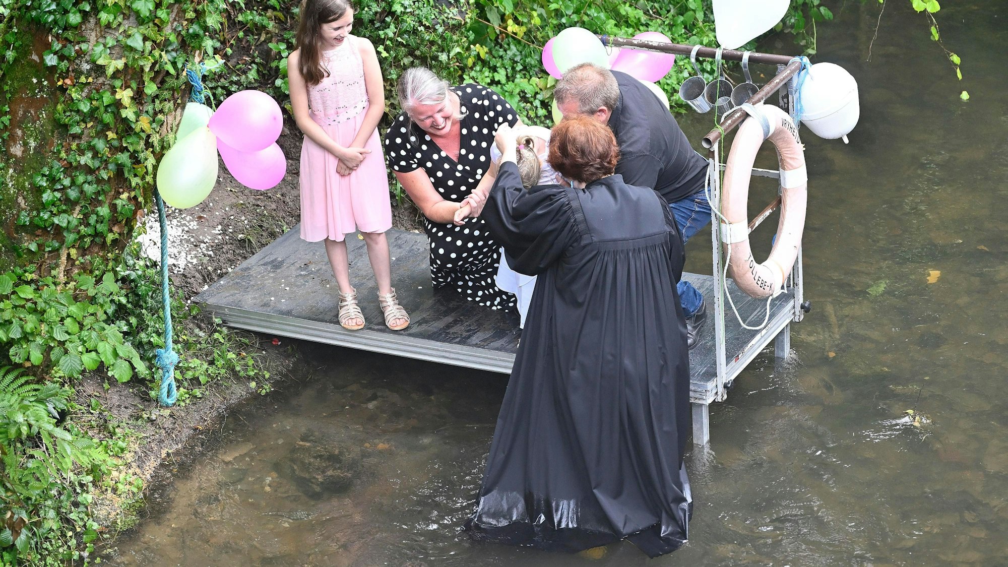 Pfarrerin Riedel mit Täufling und Familie. Die Pfarrerin steht bei der Taufe in der Dhünn.